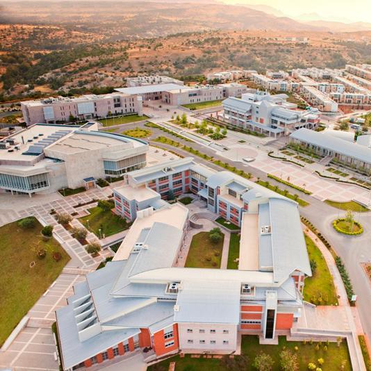 aerial view of a modern university campus with multiple academic buildings, green spaces, and surrounding hills