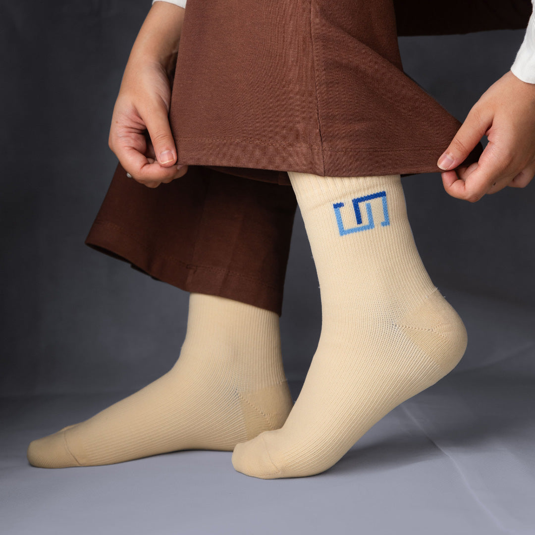 a woman wearing soft ivory color socks with a logo, brown pants, and a white shirt